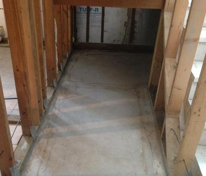 a picture of where a water heater tank was but it is removed and just the wood is exposed in the walls with cement floors.