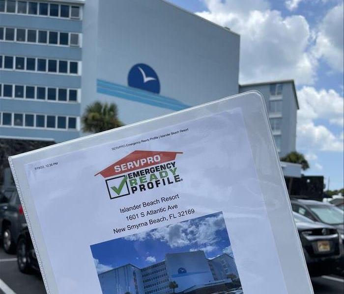 a picture of an ERP in a white binder being held in front of the blue resort that I made it for. 